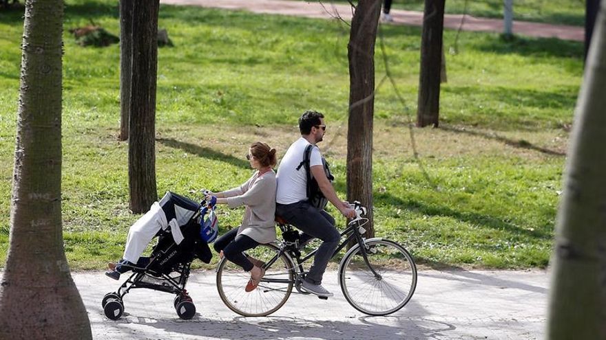 Una pareja pasea en bici con el carrito de bebé a remolque por un parque.